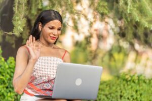 Tran woman waving at the computer while doing a video call sitting on a park